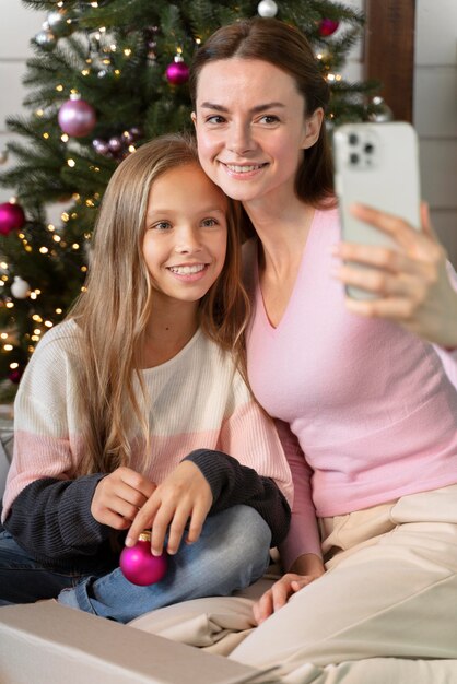 Mãe e filha tirando uma selfie perto da árvore de natal