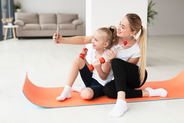 Mãe e filha tomando selfie enquanto segura pesos