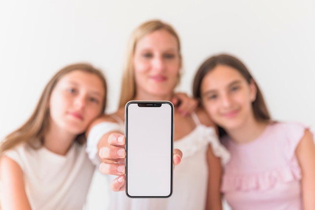 Mãe e filhas segurando smartphone com tela em branco