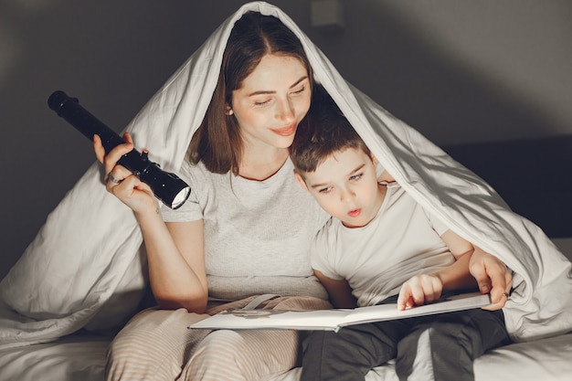 Mãe e filho debaixo do cobertor na cama lendo um livro.
