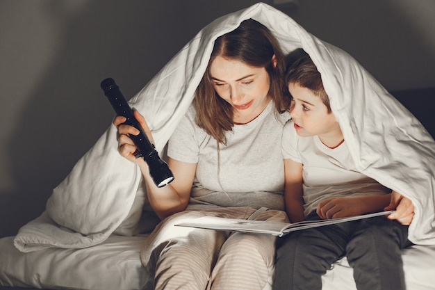 Mãe e filho debaixo do cobertor na cama lendo um livro.