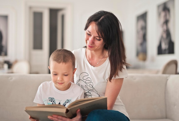 mãe e filho no sofá olham para um livro ilustrado