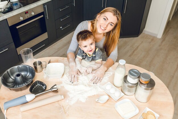 Mãe e filho sentados atrás da mesa da cozinha com coisas de cozinha nele. .