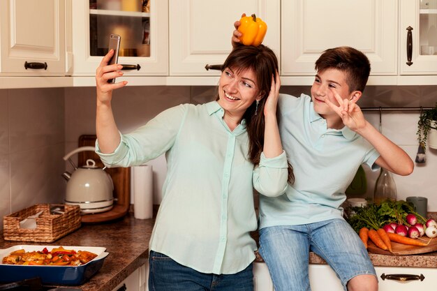 Mãe e filho tomando selfie na cozinha com legumes