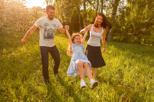 Mãe e pai balançando sua filha entre eles