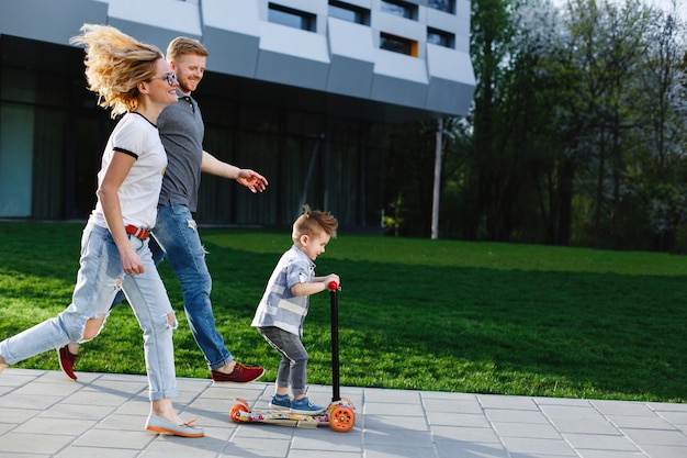 Mãe e pai correm atrás de seu filho enquanto ele monta uma scooter