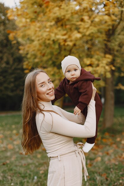 Mãe elegante com filha. Pessoas caminham lá fora. Mulher com um suéter marrom.