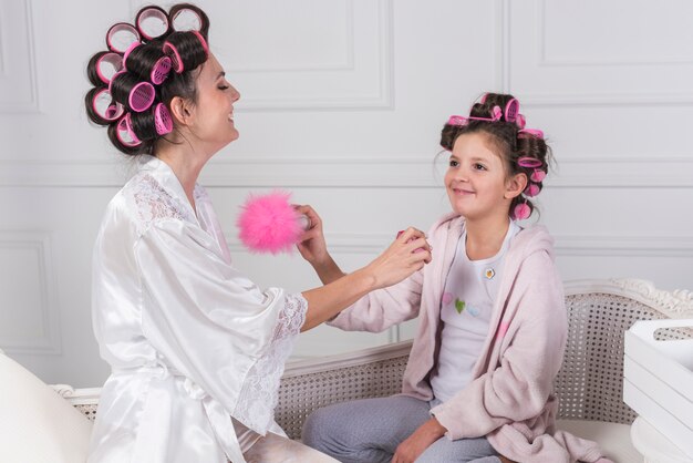 Mãe em rolos aplicando perfume no pescoço de filhas