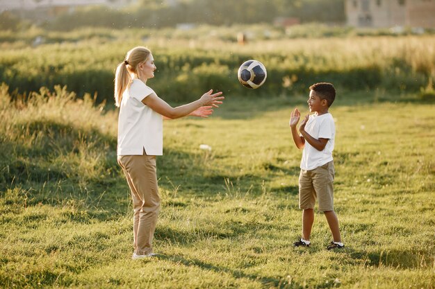 Mãe europeia e filho africano. Família em um parque de verão. As pessoas brincam com bola.