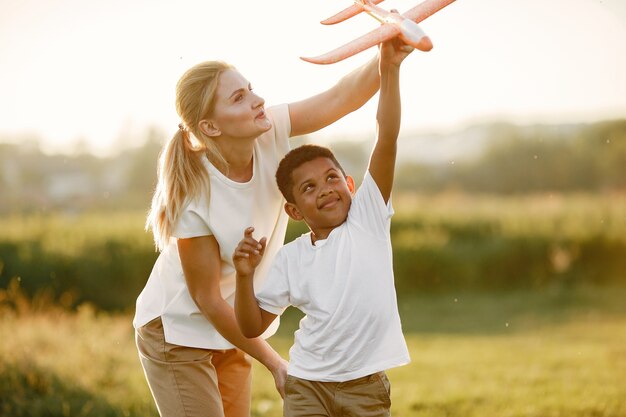 Mãe europeia e filho africano. Família em um parque de verão. As pessoas brincam com o avião.