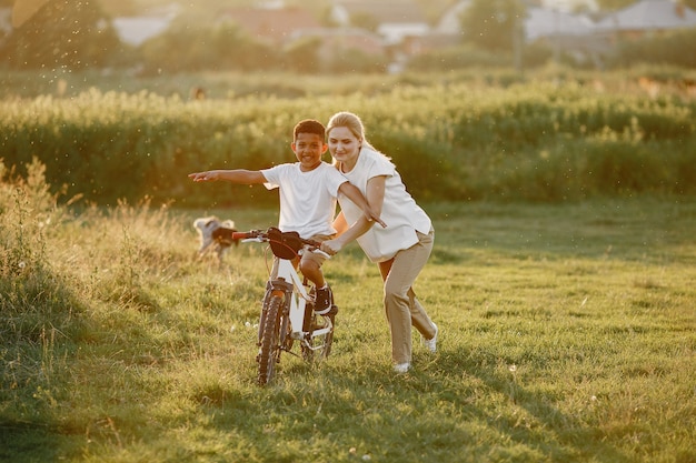 Mãe europeia e filho africano. Família em um parque de verão. Criança com bicicleta.