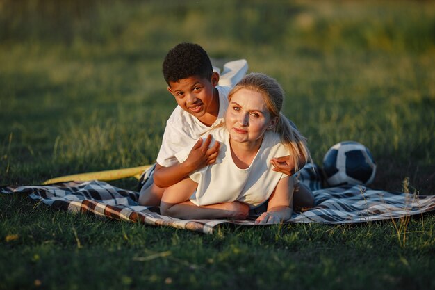 Mãe europeia e filho africano. Família em um parque de verão. Pessoas sentadas no cobertor.