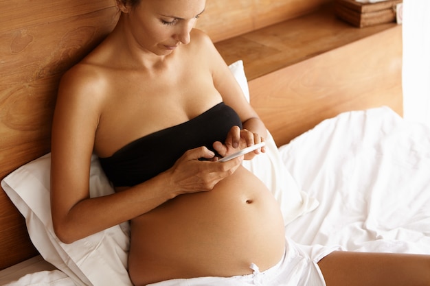 Mãe expectante bonita na parte superior cortada preta que descansa na cama