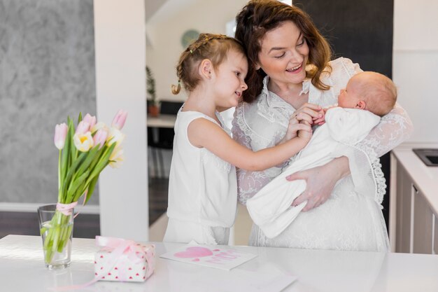 Mãe feliz com seus dois filhos bonitos em pé perto de mesa branca