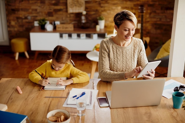 Mãe feliz usando touchpad e laptop enquanto está com a filha em casa