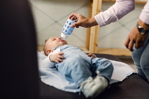 Mãe irreconhecível alimentando seu filho que está deitado no sofá