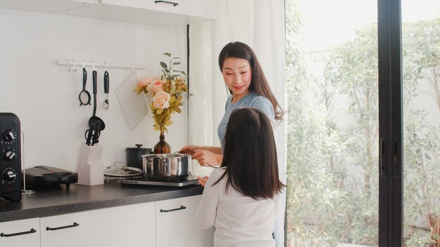 Mãe japonesa asiática nova e filha que cozinham em casa. Mulheres do estilo de vida felizes fazendo macarrão e espaguete junto para a refeição do café da manhã na cozinha moderna em casa de manhã.