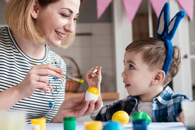 Mãe loira ensinando seu filho a pintar ovos para a Páscoa