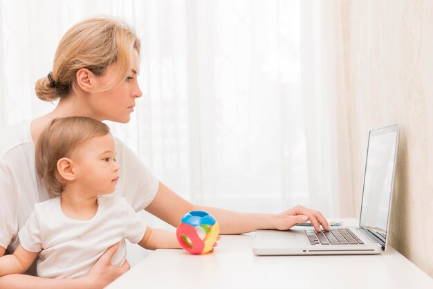 Mãe meados de tiro segurando bebê trabalhando na mesa