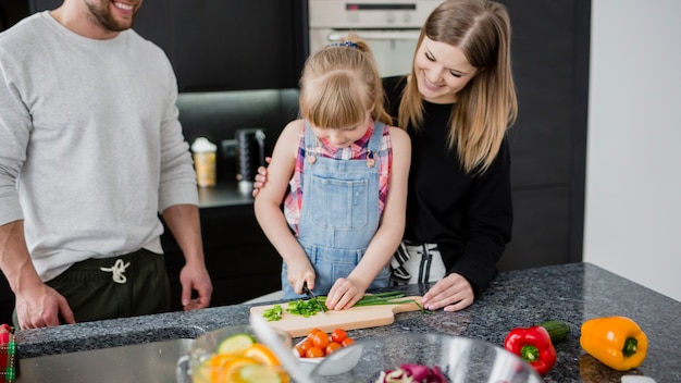 Foto grátis mãe pai ajudando a filha a cortar legumes