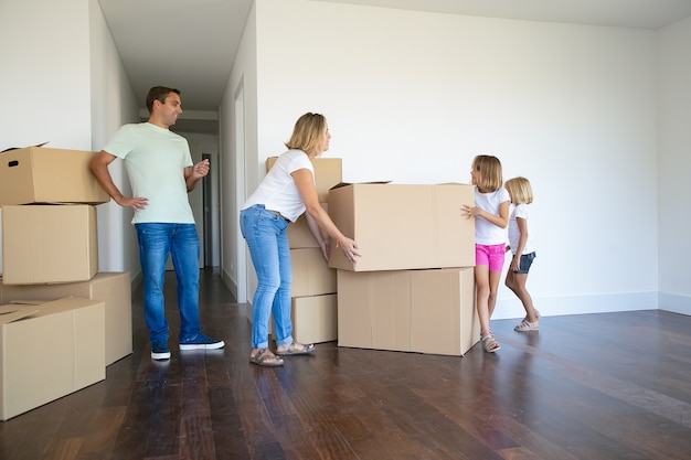 Mãe, pai, duas meninas carregando caixas e empilhando em seu novo apartamento vazio