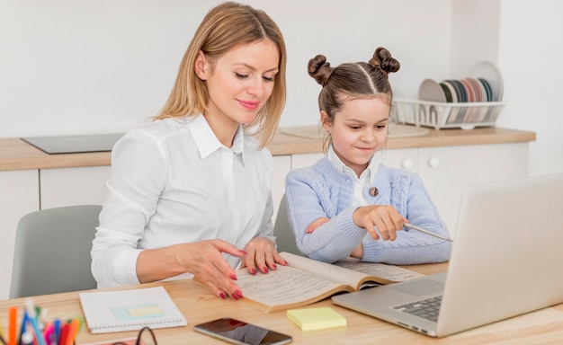 Mãe sorridente, ajudando a filha em uma aula on-line