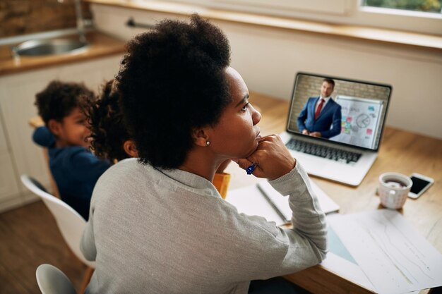 Mãe trabalhadora afro-americana pensativa tendo reunião on-line sobre laptop em casa