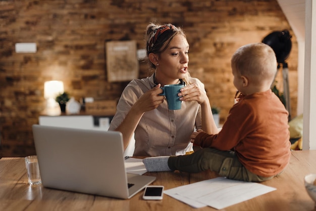 Mãe trabalhadora conversando com seu filho pequeno enquanto toma uma xícara de café em casa
