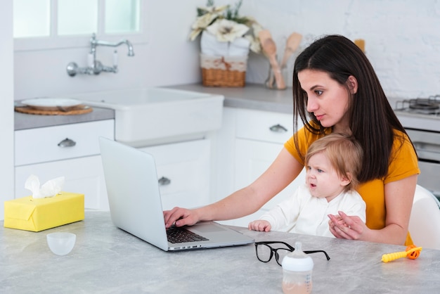 Mãe trabalhando no laptop, segurando o bebê