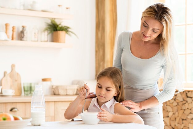 Mãe vendo sua filha tomar café da manhã