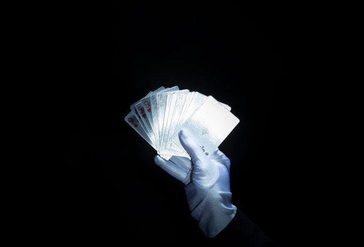 Foto grátis magician&#39;s hand wearing white luva segurando ventilado cartas de jogar contra o fundo preto