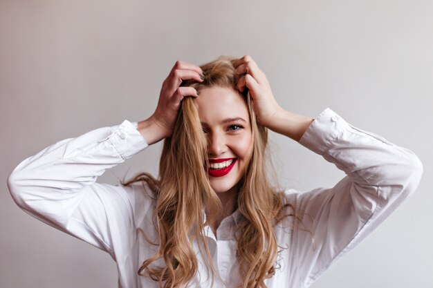 Magnífica jovem garota tocando o cabelo loiro com um sorriso. elegante modelo feminino na camisa.