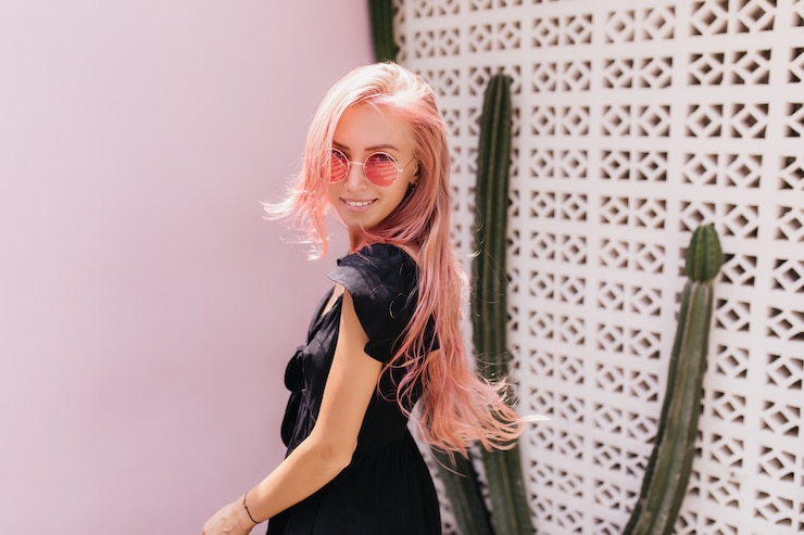 Foto grátis magnífica mulher com cabelo rosa posando em frente a um cacto e sorrindo.
