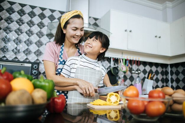 Mamã feliz que ensina sua filha que prepara e que desbasta o vegetal para cozinhar.