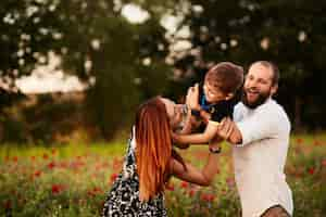 Foto grátis mamãe e papai segurar seu filho nos braços de pé no campo verde com papoulas