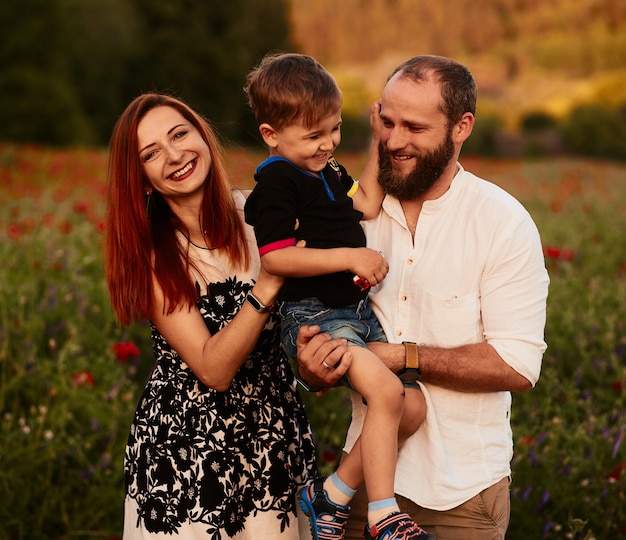 Mamãe e papai segurar seu filho nos braços de pé no campo verde com papoulas