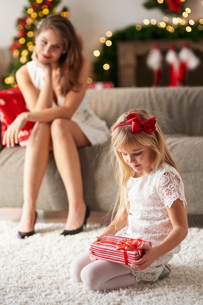 Mamãe observando a filha enquanto abre os presentes