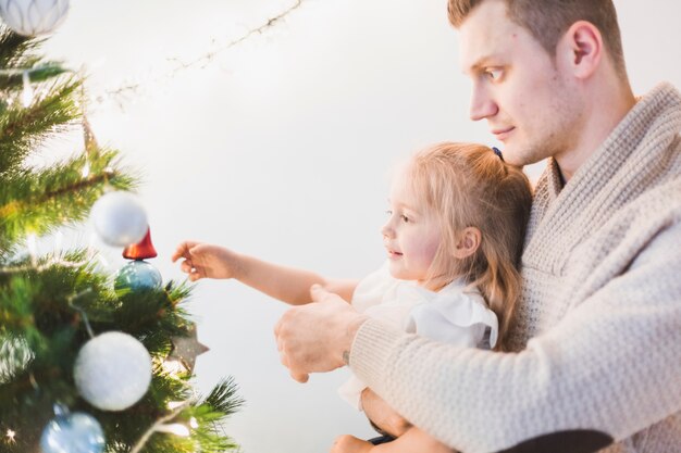Man e criança decorando árvore de Natal iluminada