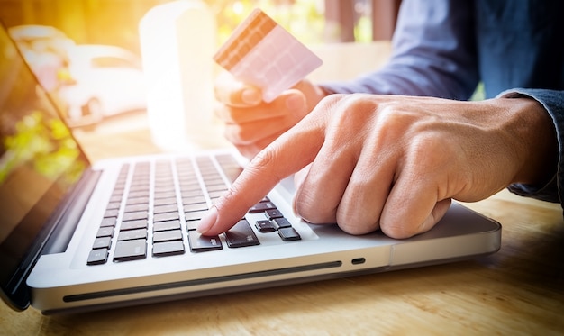 Man segurando cartão de crédito na mão e inserindo código de segurança usando o teclado do laptop