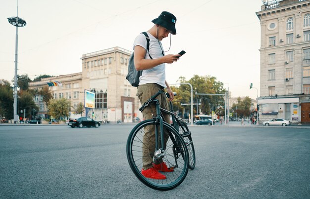 Mandava um jovem elegante telefone ao pé de bicicleta de lado.