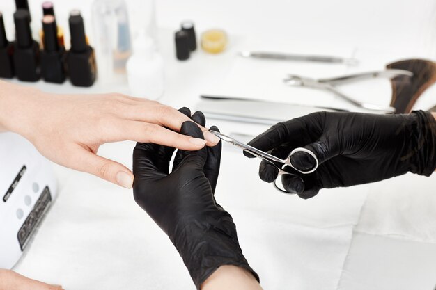 Manicure profissional em luvas pretas, corte a cutícula com uma tesoura de manicure.