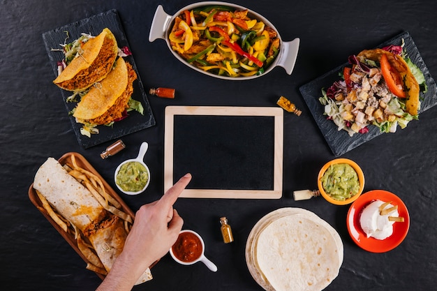 Mão apontando no quadro negro em meio à comida mexicana