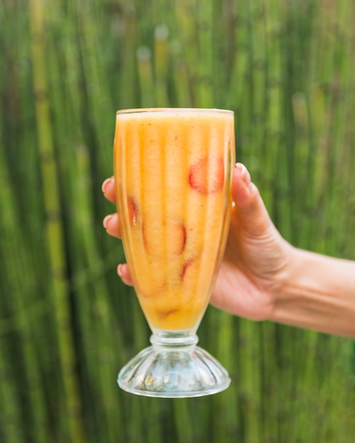 Foto grátis mão com copo de suco fresco perto de bambu