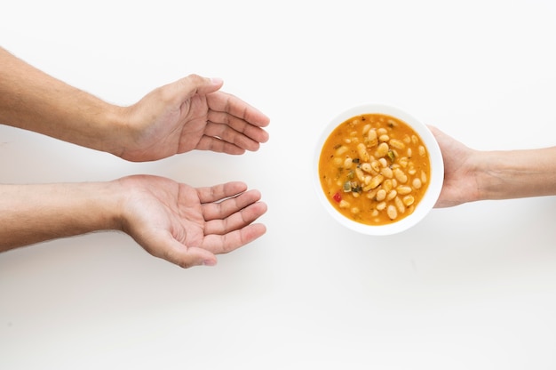 Mão dando tigela de sopa para pessoa necessitada