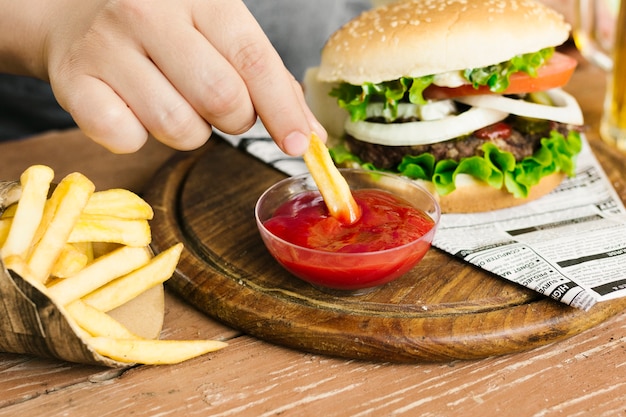 Mão de close-up de ângulo alto mergulhando fritas com hambúrguer
