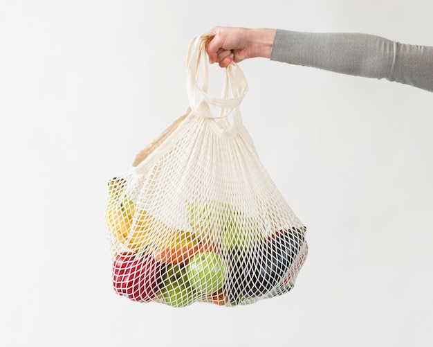 Mão de close-up, segurando o saco reutilizável com legumes e frutas