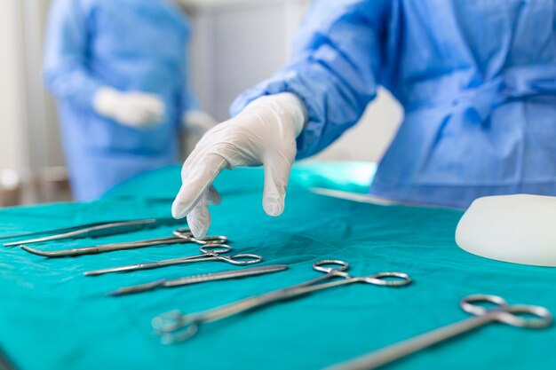 Mão de enfermeira tomando instrumento cirúrgico para grupo de cirurgiões no paciente operando em segundo plano no teatro cirúrgico Instrumentos médicos de aço prontos para serem usados Conceito de cirurgia e emergência