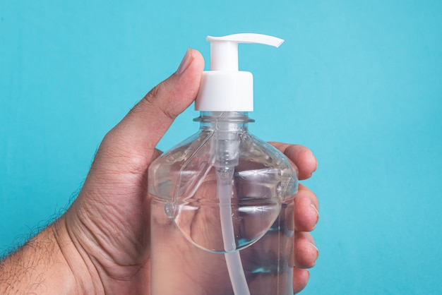 Mão de homem em recipiente com gel de álcool na luz azul