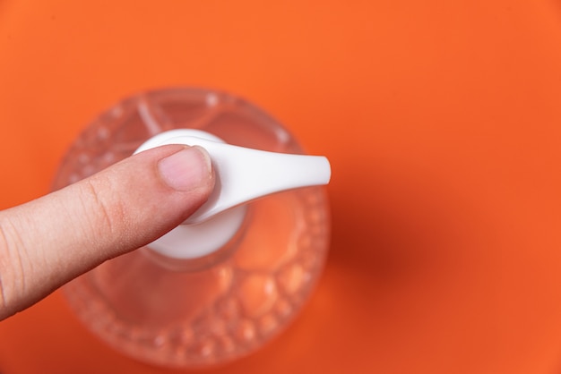 Mão de homem em recipiente com gel de álcool na parede laranja