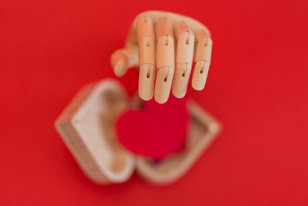 Mão de madeira com coração vermelho na mesa